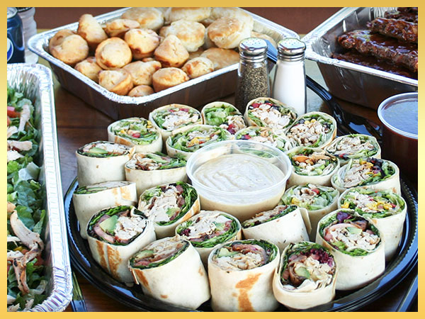 Catering platter with chicken wraps, garden salad, and muffins.